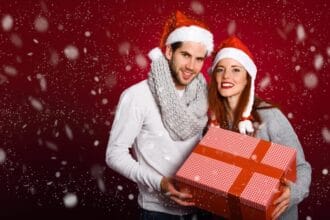 couple-with-christmas-gift-dressed-with-winter-clothes-santa-hat-snow-red-background_23-2147576866
