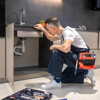 man-kneeling-down-touching-sink-inspecting-pipes_259150-58251
