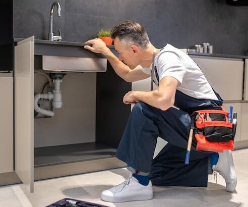 man-kneeling-down-touching-sink-inspecting-pipes_259150-58251